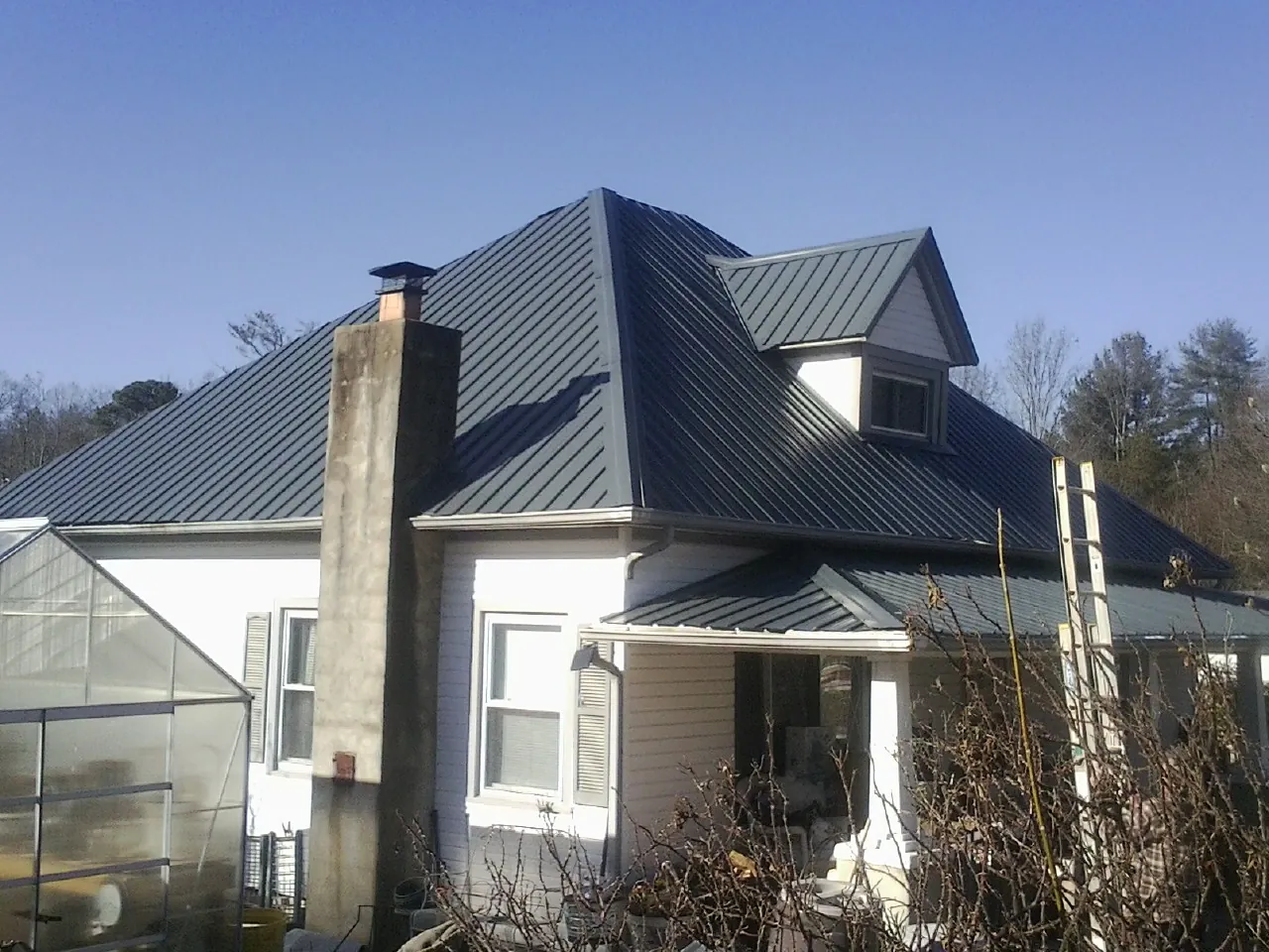 Dark blue standing seam metal roof on a white farmhouse with dormer — Slate & Tile Roof Repair by Roofing Brothers in Ledbetter
