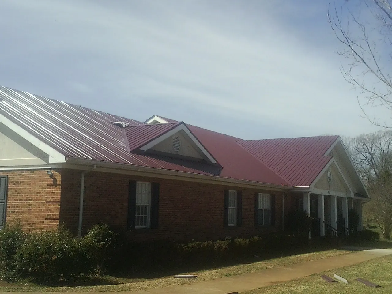Red metal roof with gabled entries on a long brick building, from a Hail Damage Roof Repair job in Ledbetter
