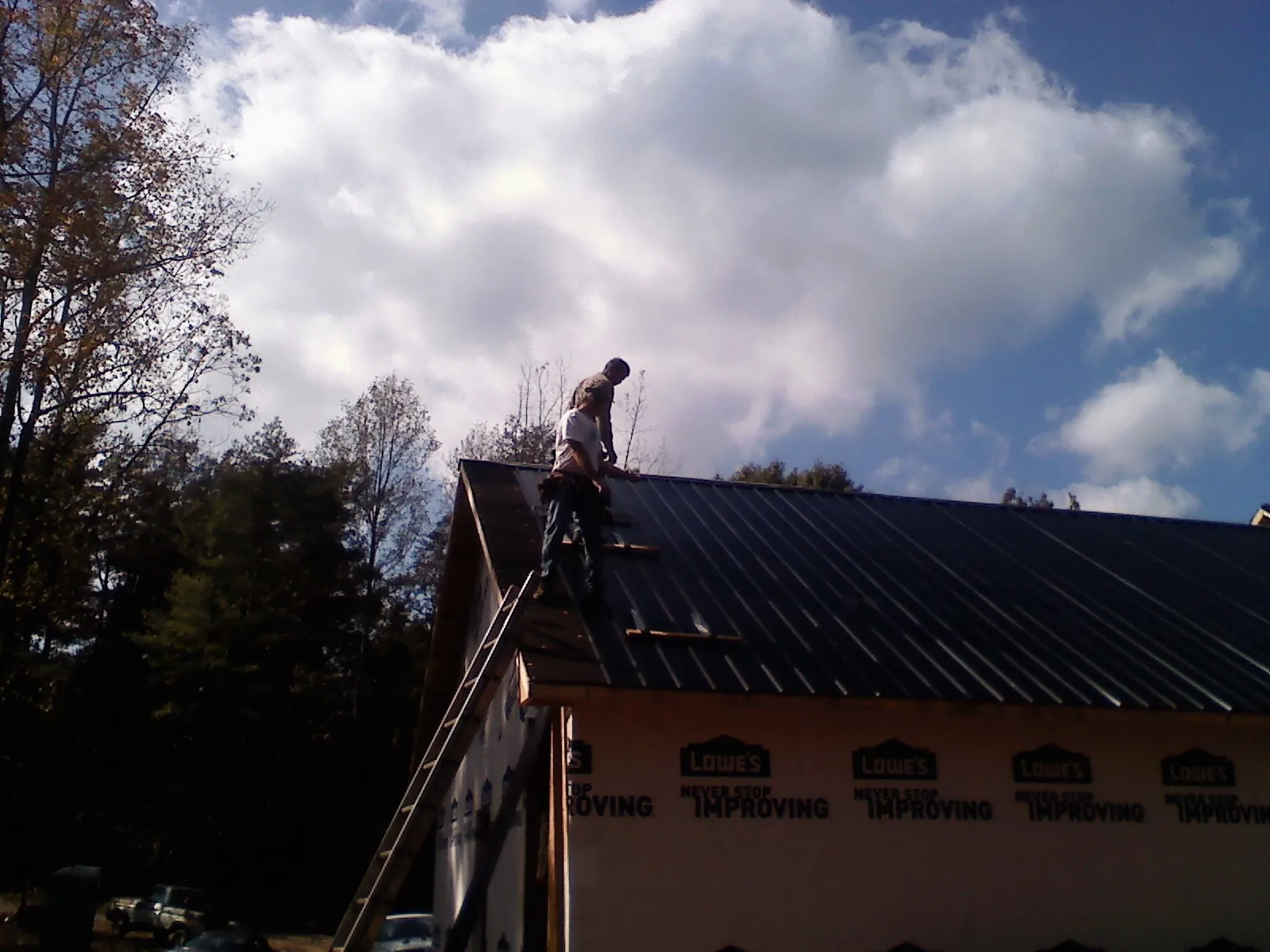 Roofer fastening dark metal panels high against a cloudy sky, from a Roof Inspection job in Ledbetter